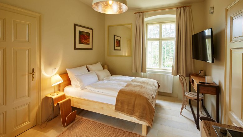 Útulná ložnice s manželskou postelí, psacím stolem a velkým oknem.