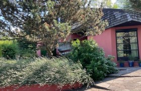 Ein modernes Haus mit roter Fassade, umgeben von Bäumen und Sträuchern.