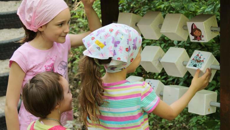 Drei Kinder spielen an einem hölzernen Spielgerät im Freien.