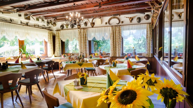 Gemütlicher Gastraum mit Holzmöbeln, gelben Tischdecken und Sonnenblumen.