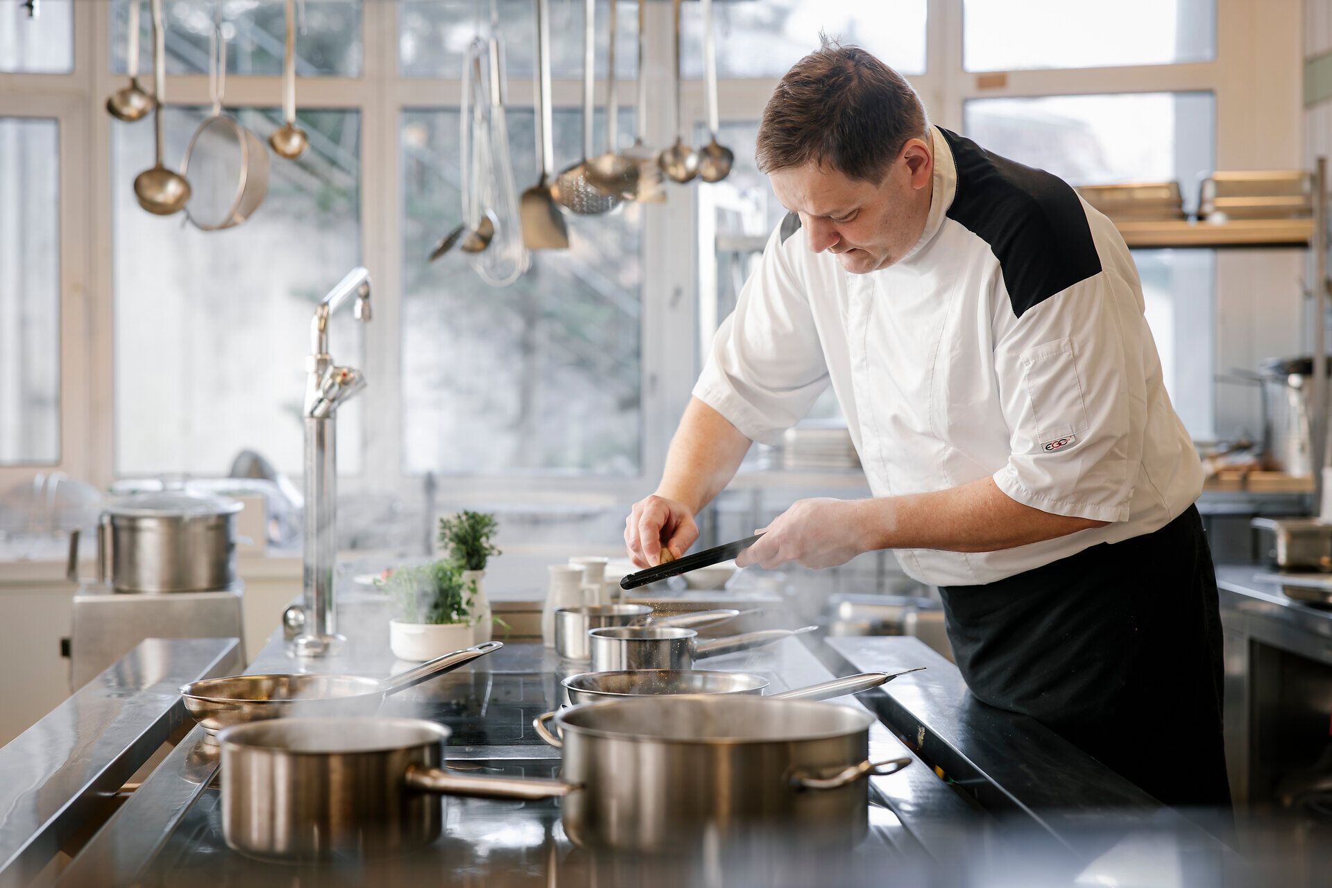 Koch steht in einer professionellen Küche, reibt etwas in einen Topf.