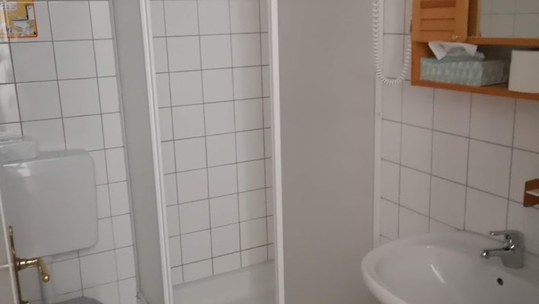 Ein kleines, weiß gefliestes Badezimmer mit Dusche, Toilette und Waschbecken.