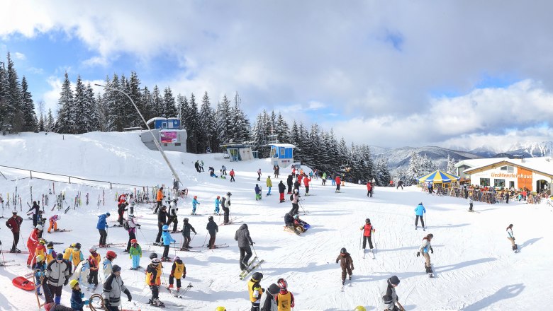 Skigebiet mit vielen Menschen, Sessellift und Berglandschaft.