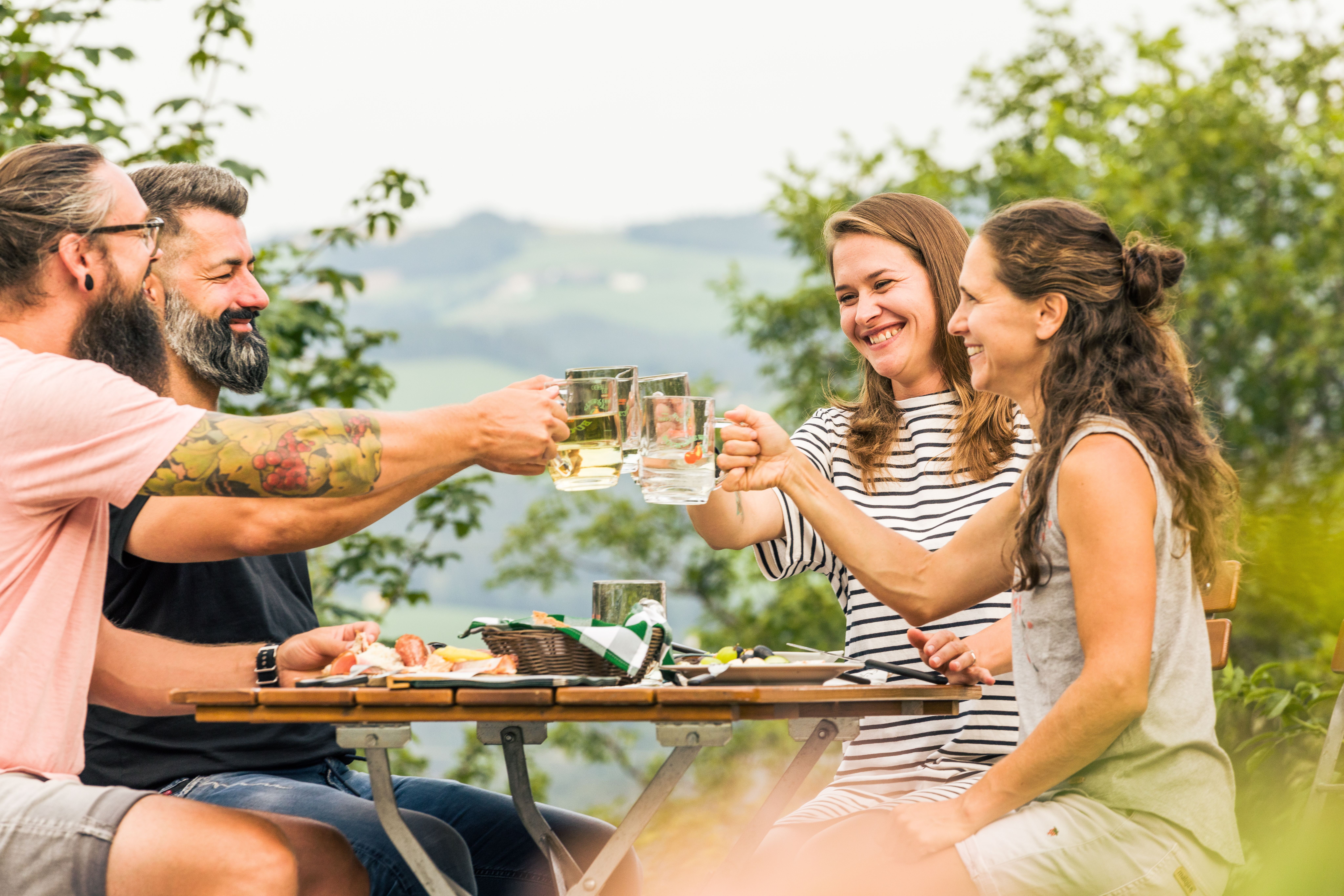 Vier Personen sitzen an einem Tisch im Freien und stoßen mit Mostgläsern an.