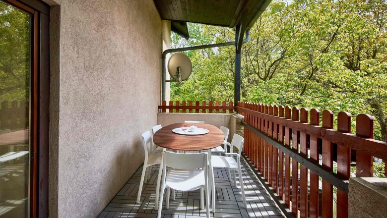 A balcony with a wooden table, white chairs and a view of green trees.