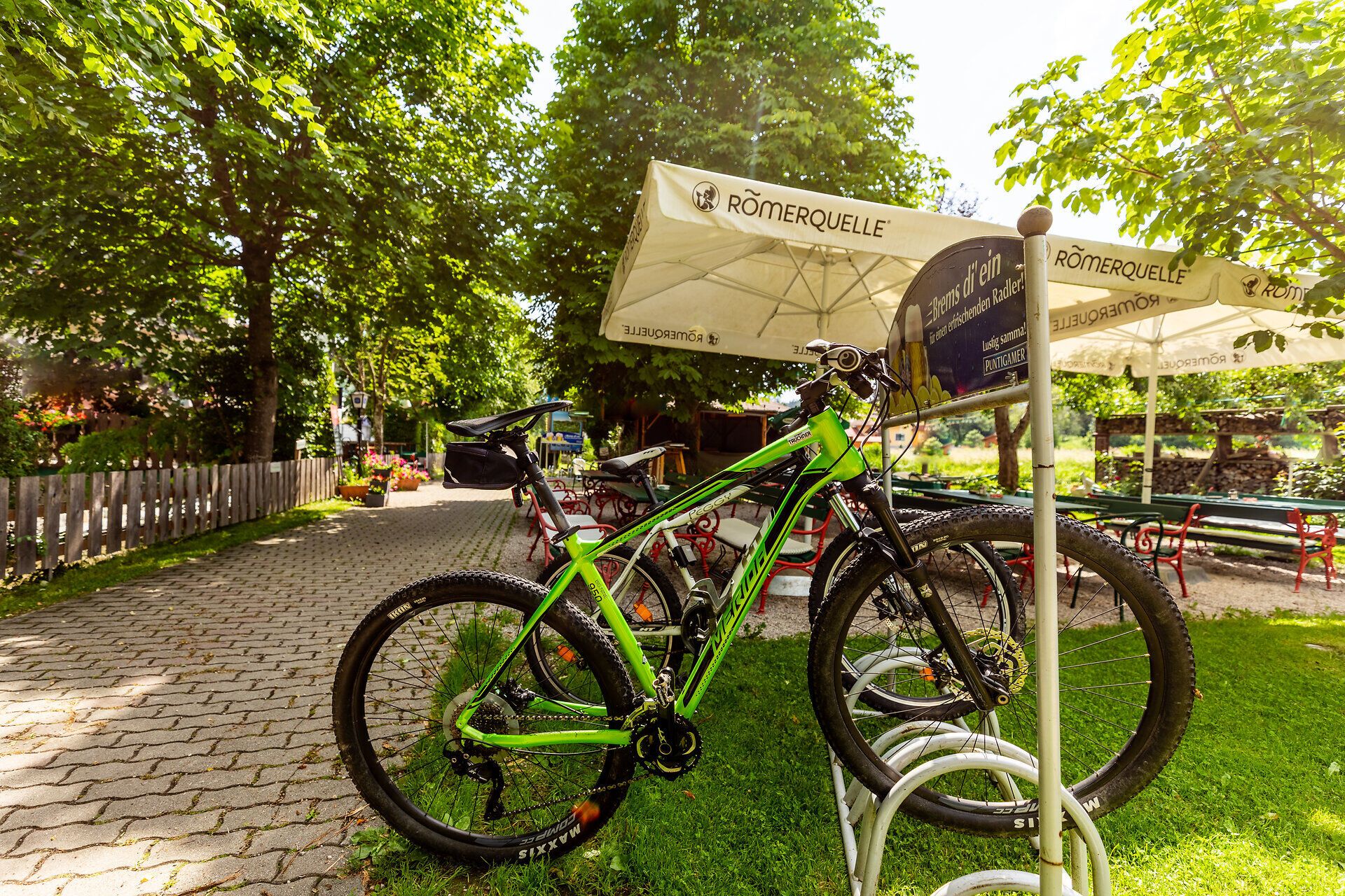 Am Radständer im grünen Gastgarten vom Gasthof Pension St. Wolfgang sind zwei Fahrräder geparkt.