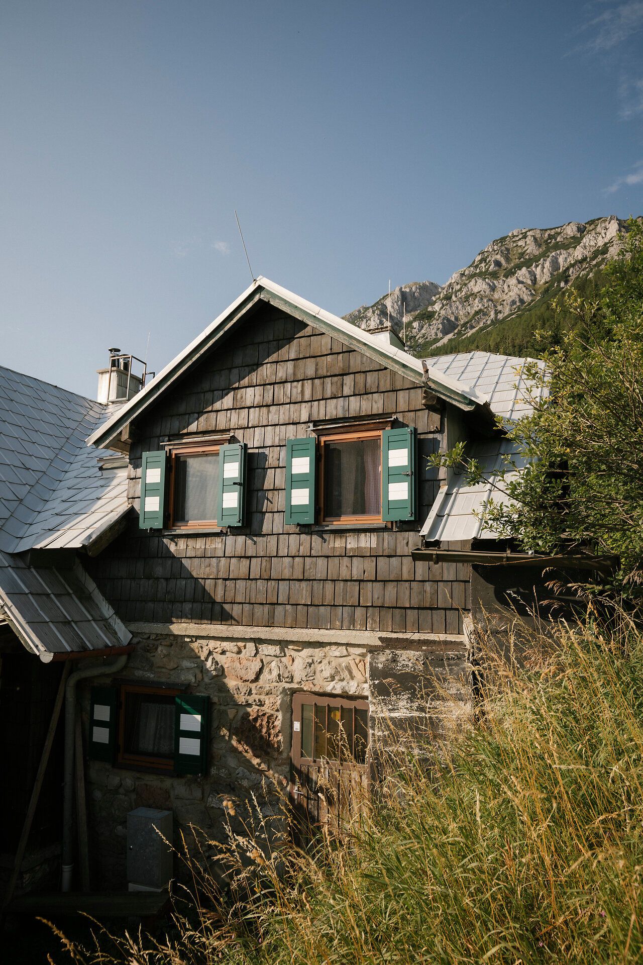 Außenansicht der Edelweißhütte am Schneeberg mit Schindelfassade und grünen Fensterläden