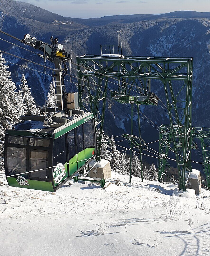 Die Rax-Seilbahn schwebt majestätisch über die schneebedeckten Hänge, während die winterliche Landschaft in strahlendem Weiß erstrahlt. Die frische Bergluft und die glitzernden Schneekristalle schaffen eine zauberhafte Atmosphäre, die zum Erkunden einlädt.
