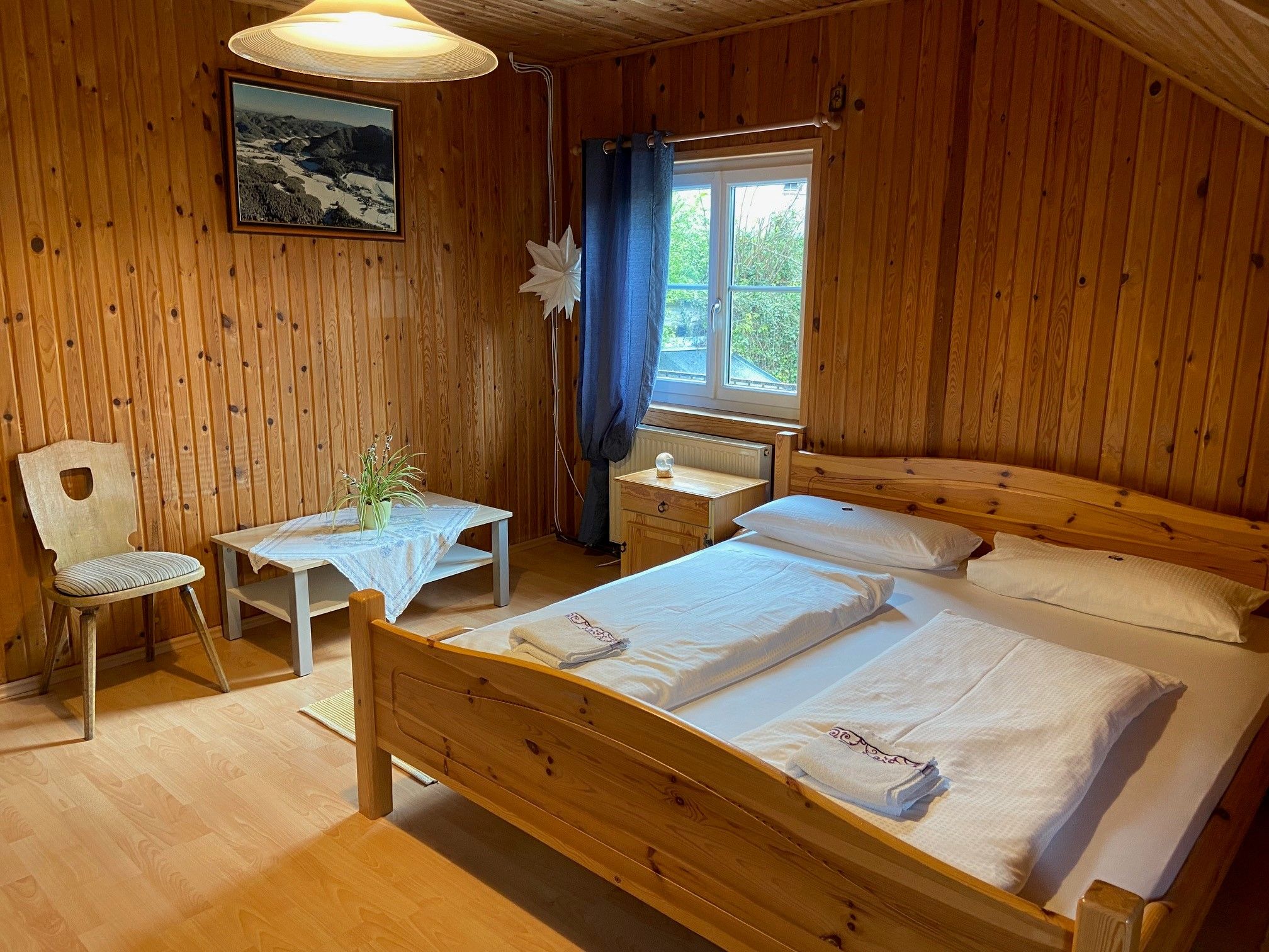Holzvertäfeltes Doppelzimmer mit Bett, Tisch, Stuhl und Fenster.