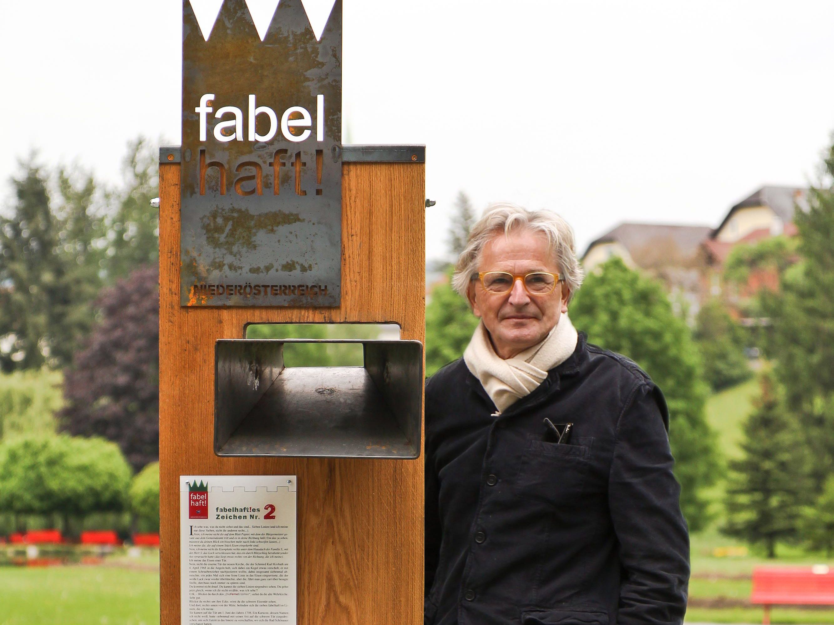Ein Mann steht neben einem Holzschild mit der Aufschrift 'fabelhaft!' in einem Park.