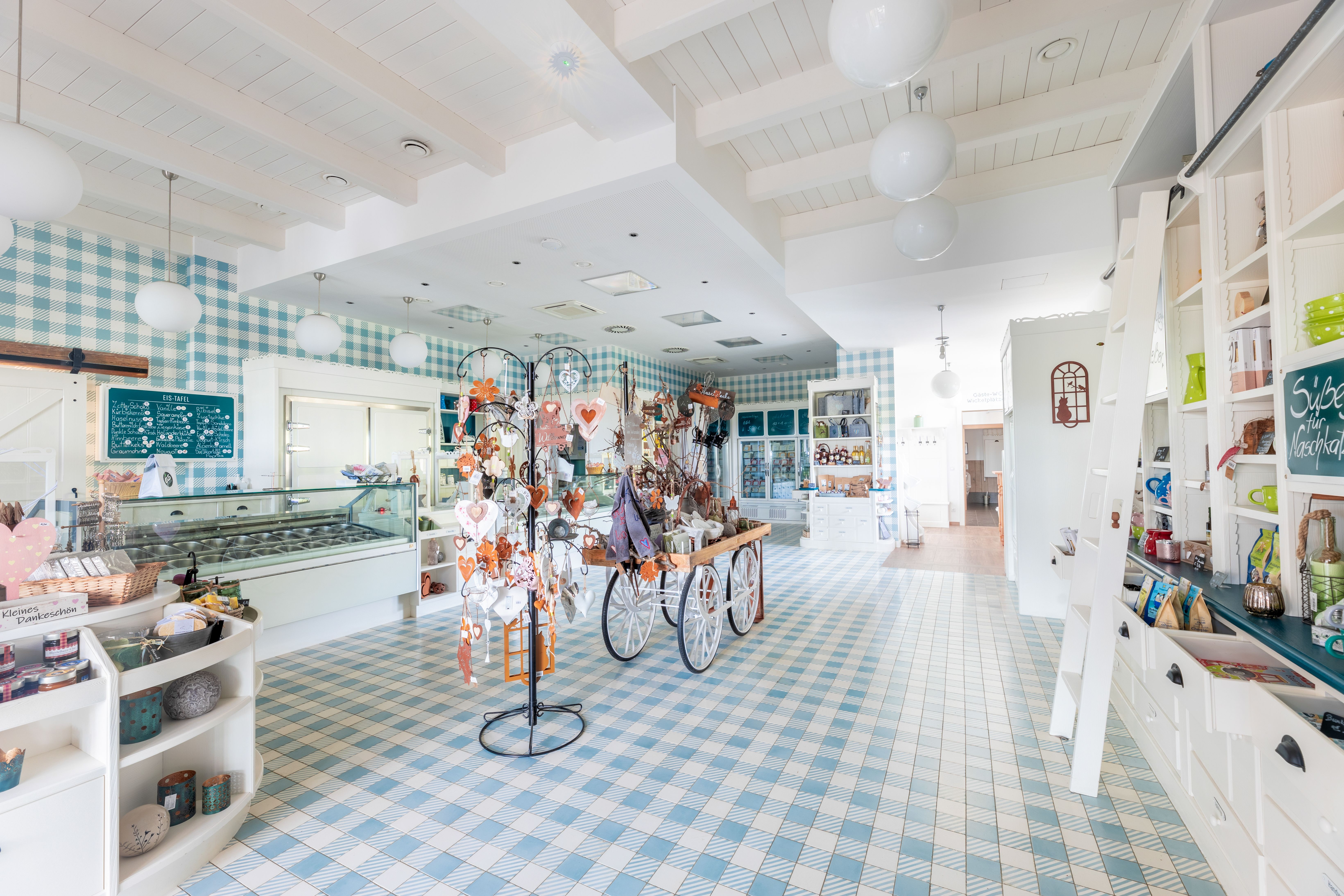 Innenansicht eines Hofladens mit karierten Wänden, einer Eisvitrine, weißen Regalen und regionalen Produkten.