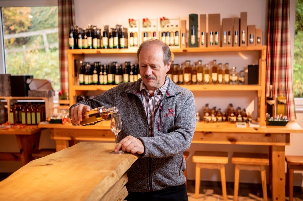 Mann steht an einer Theke aus Holz und gießt Schnaps in ein Schnapsglas.