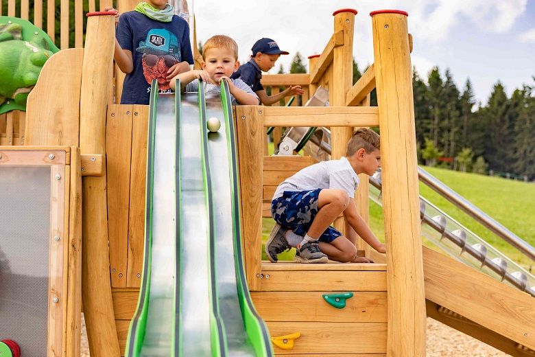 Kinder spielen auf einem Holzspielplatz mit einer Kugelbahn.