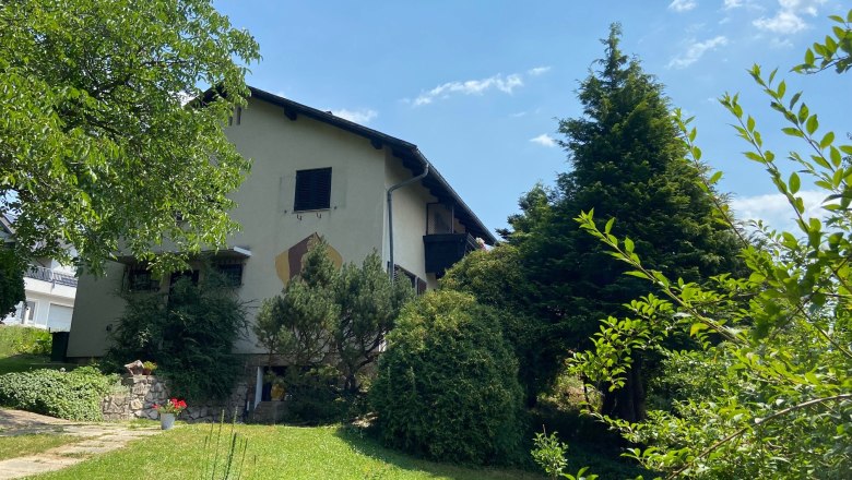 Ein zweistöckiges Haus mit Garten und Bäumen, bei sonnigem Wetter.