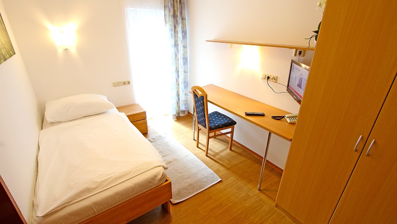Ein einfach eingerichtetes Einzelzimmer mit Bett, Schreibtisch, Stuhl und Fernseher.