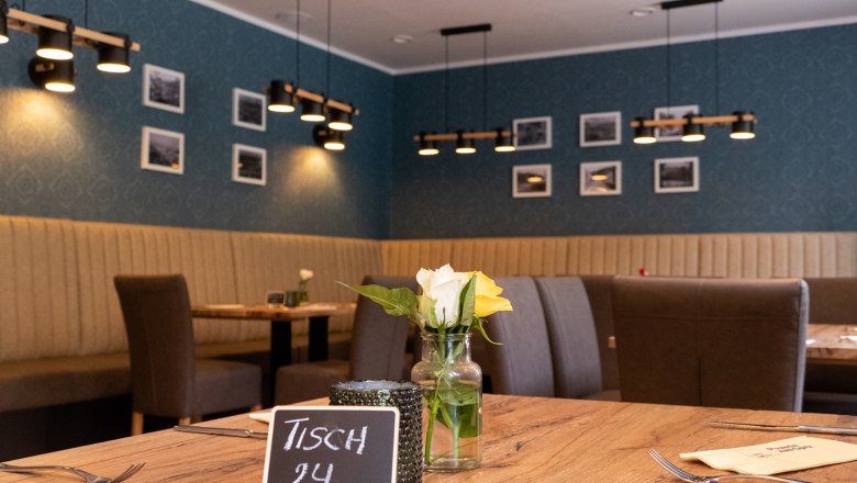 Innenansicht eines Restaurants mit Holztisch, Blumen und moderner Beleuchtung.