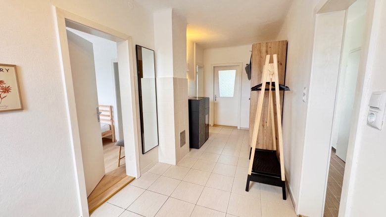 Heller Flur mit Fliesenboden, Spiegel, Garderobe und Türen zu angrenzenden Räumen.