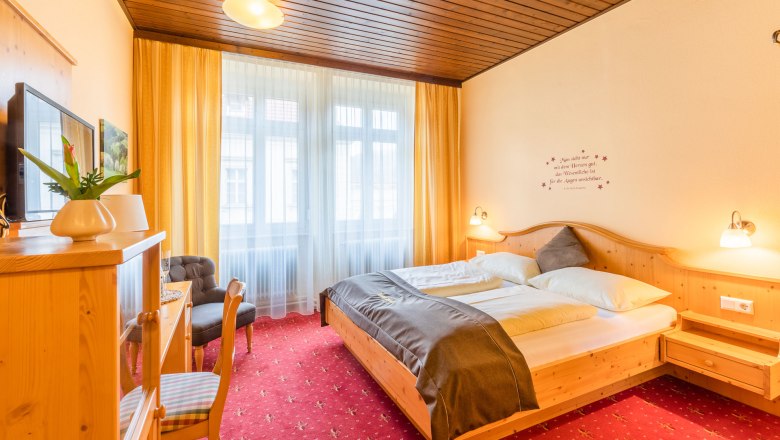 Gemütliches Hotelzimmer mit Doppelbett, Holzmöbeln und rotem Teppich.