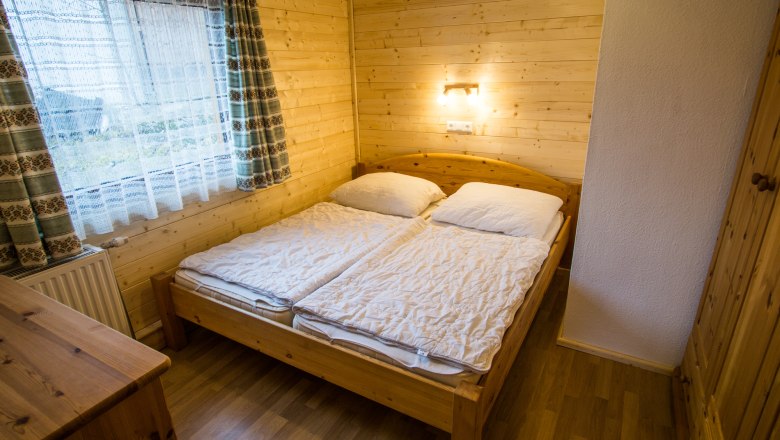 Gemütliches Schlafzimmer mit Holzwänden, Doppelbett und Fenster mit Vorhängen.