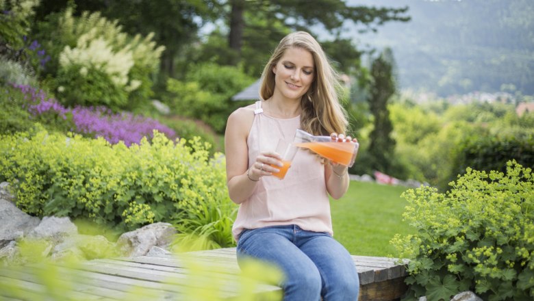 Woman sits in the garden and pours juice into a glass.