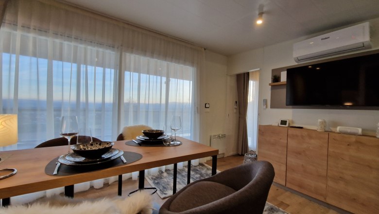 Modernes Wohnzimmer mit Esstisch, Stühlen, großem Fenster und Fernseher.