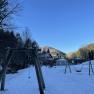 Snow-covered playground with swings, surrounded by trees and mountains under a clear blue sky.