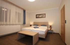 Ein schlicht eingerichtetes Zimmer mit Doppelbett, Holzmöbeln und Vorhängen.