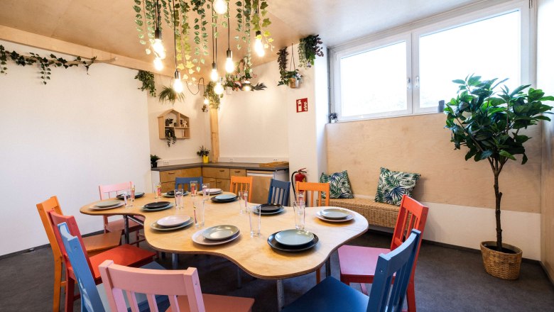 Ein gemütlicher Raum mit einem Tisch, umgeben von bunten Stühlen und Pflanzen.
