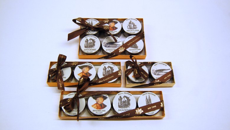 Three golden boxes with round, printed sweets, decorated with brown bows.