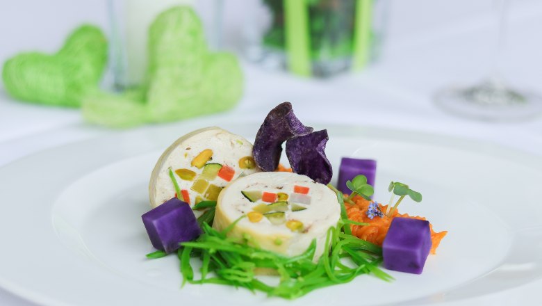 Artfully arranged corn roulade, purple potato cubes and green garnish on a white plate.