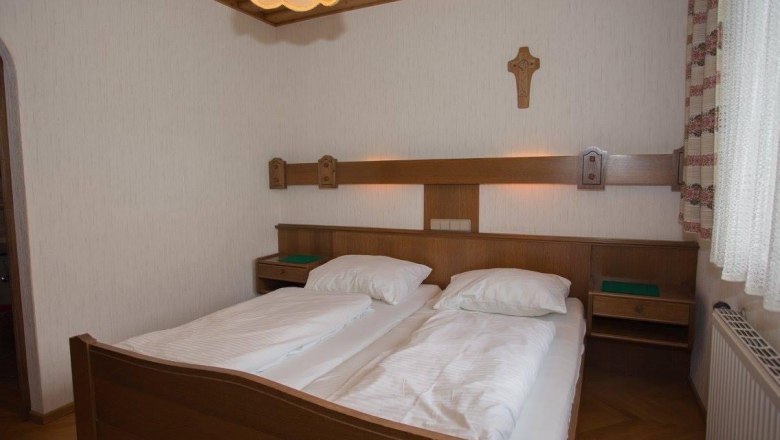 Ein traditionelles Doppelzimmer mit Holzmöbeln, zwei Betten, einem Kreuz an der Wand und einer Lampe an der Decke.