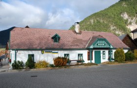 Schneeberg Museum Puchberg, a traditional building with a green roof and chimney, surrounded by mountains and trees.