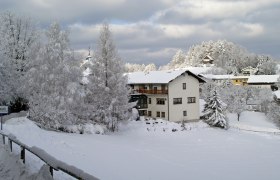 Winterlandschaft mit verschneitem Gasthof und Bäumen.