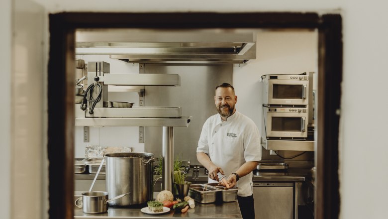 Ein Koch in einer professionellen Küche, der lächelnd Gemüse schneidet.