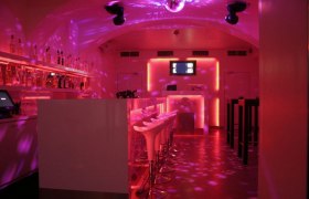 Innenansicht eines Clubs mit Bar, rosa Beleuchtung und Disco-Kugel.