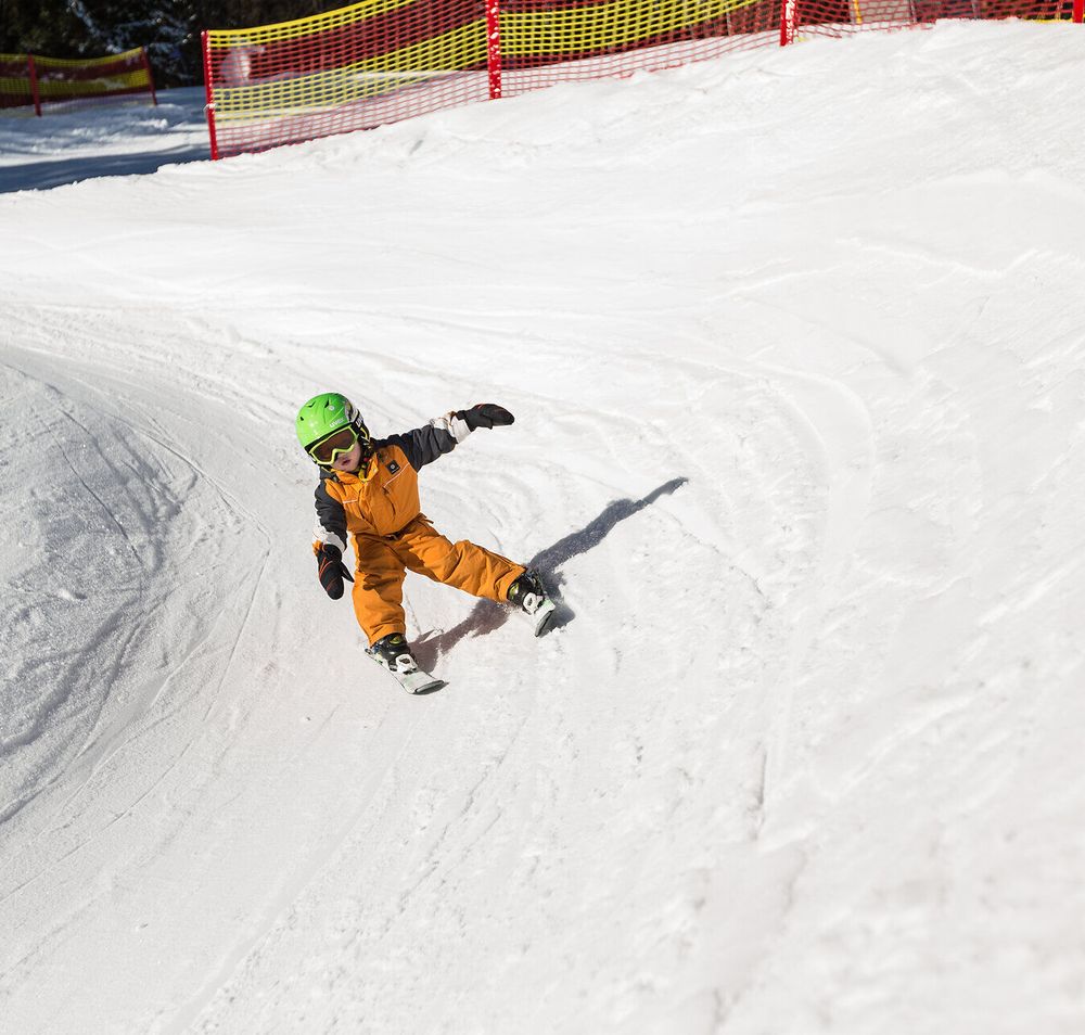 Ein kleiner Skifahrer gleitet mit Freude über die schneebedeckte Piste und genießt die winterliche Freiheit. Die strahlende Sonne und die frische Bergluft schaffen eine perfekte Kulisse für unvergessliche Familienmomente im Schnee.