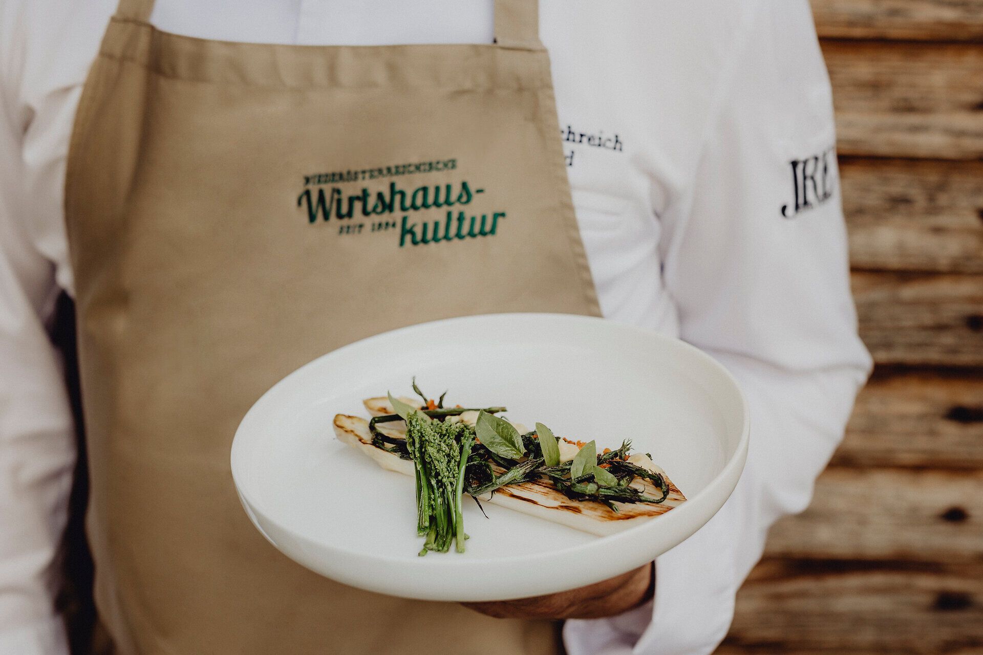 Ein kunstvoll angerichteter Teller mit gegrilltem Marchfeld-Spargel und wilder Hopfenspargel lädt zu einem kulinarischen Erlebnis ein. Die frischen, grünen Aromen versprechen einen Genuss, der die Sinne verzaubert und die Schönheit der Wiener Alpen widerspiegelt.