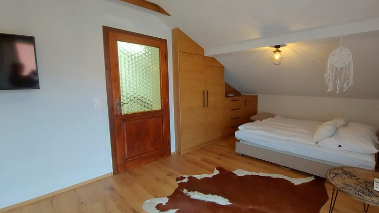 Schlafzimmer mit Holzboden, Bett, Schrank, Tür und Fernseher.