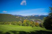 Blick auf eine gr&uuml;ne Landschaft mit H&uuml;geln und Bergen im Hintergrund, unter einem klaren blauen Himmel.