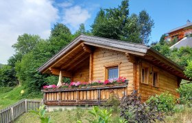 Holzhütte mit Blumen auf der Veranda in einer grünen Umgebung.