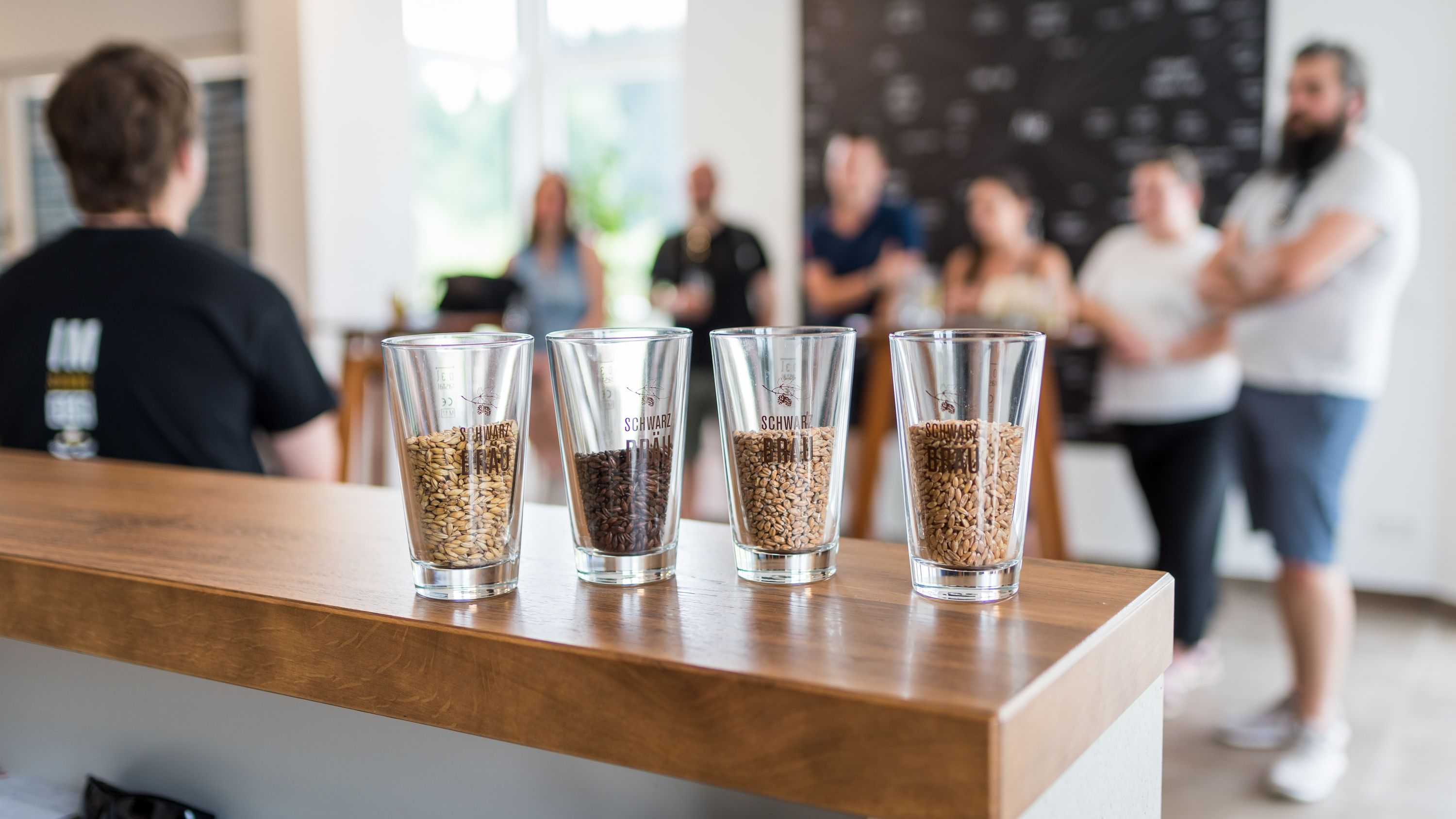 Nahaufnahme von Schnapsgläsern mit diversen Getreidekörnern auf einer Holztheke.