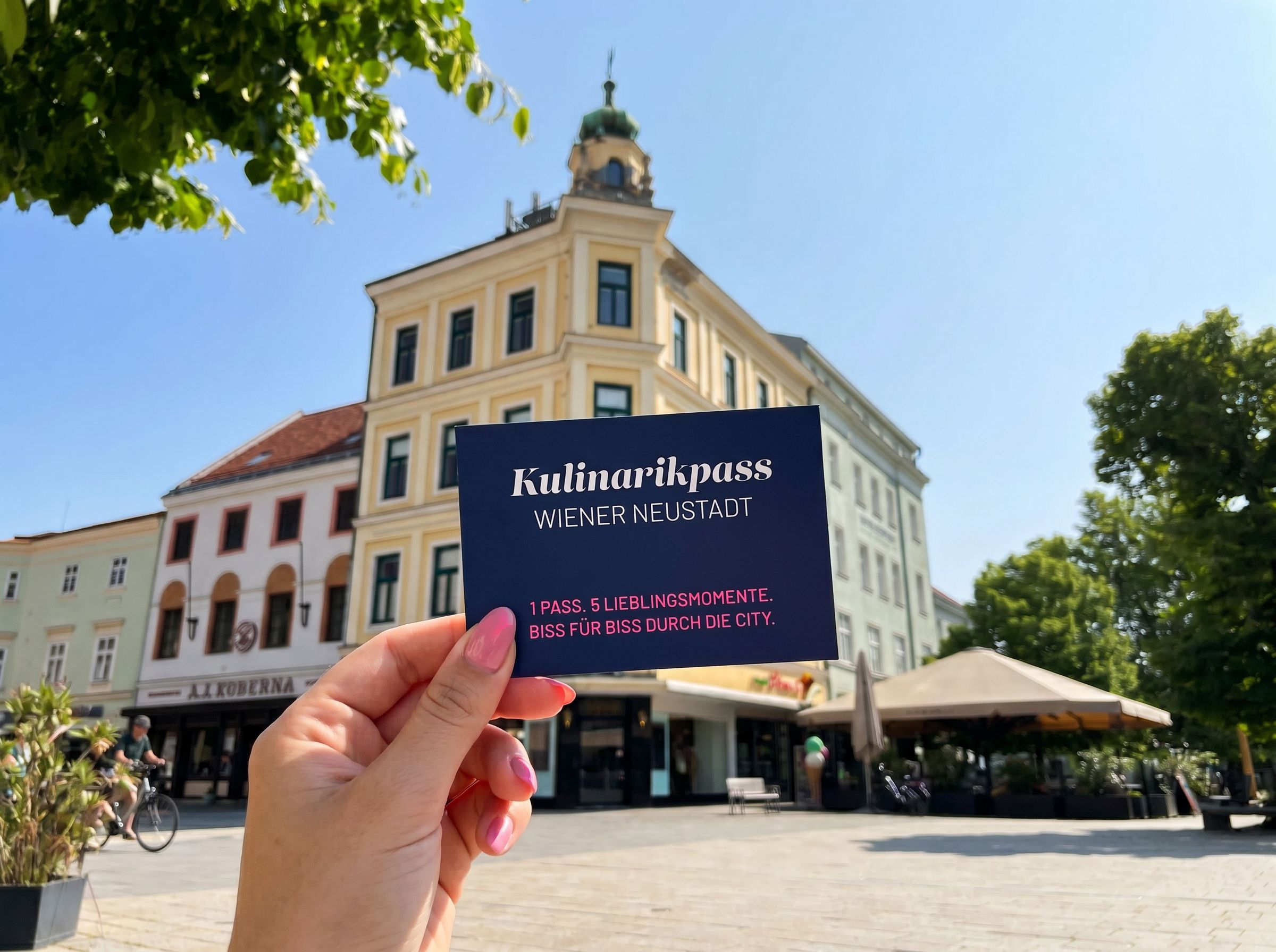 Kulinarikpass, der von einer Hand am Hauptplatz gezeigt wird