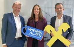  Dir. Johann Sperhansl (Raiffeisenbank Region Wiener Alpen), Wiener Alpen Geschäftsführerin Mariella Klement-Kappeller & Dir. Hannes Wedl (Raiffeisenbank Region Wiener Alpen) stehen für ein Gruppenbild nebeneinander und halten ein Wiener Alpen-Logo-Schild sowie ein Raiffeisen-Logo Schild in den Händen  