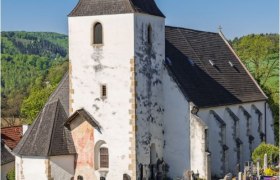 Rustikale Wehrkirche Bromberg mit breitem Turm und Friedhof im Vordergrund.