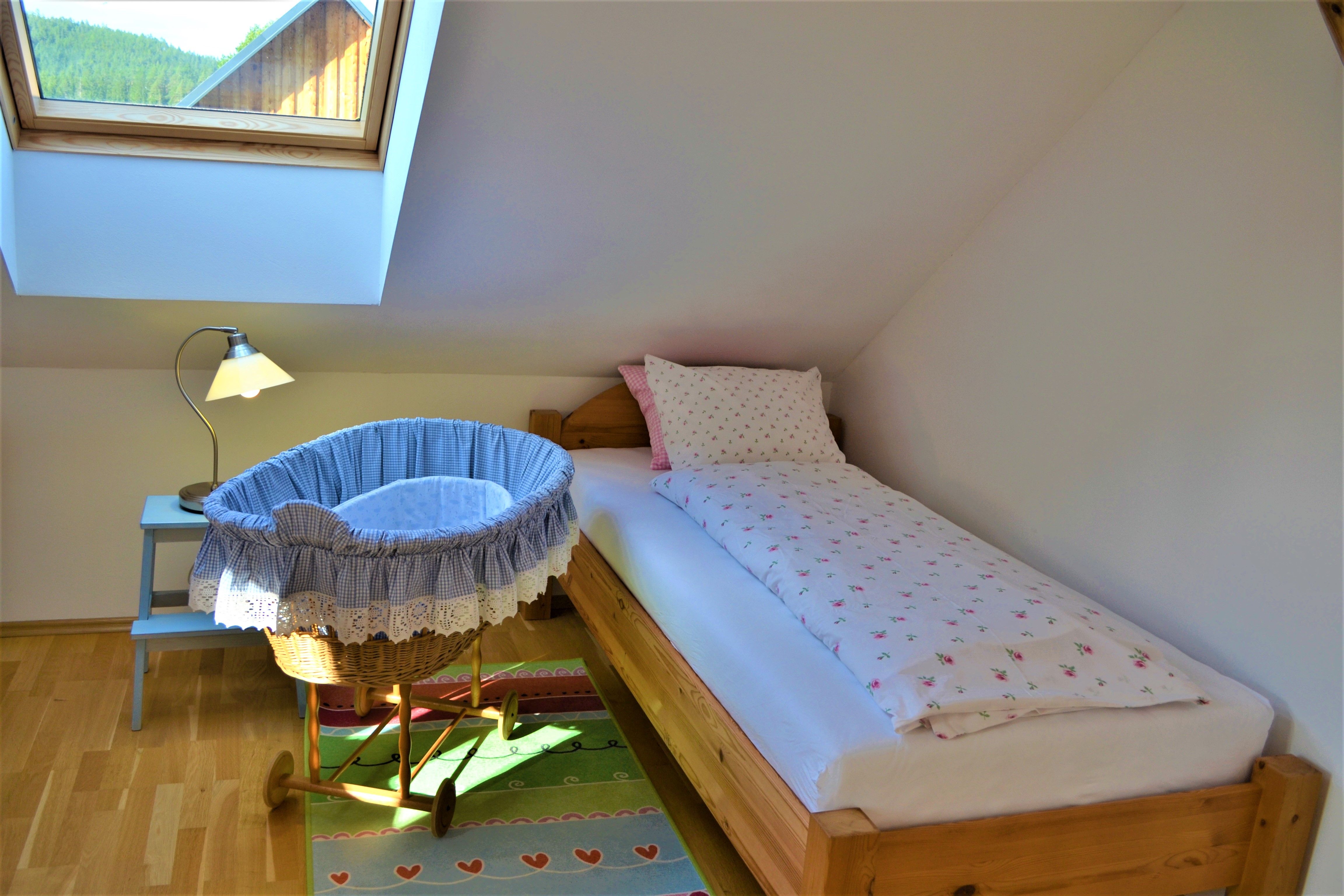 Ein gemütliches Schlafzimmer mit Einzelbett, Babywiege und Dachfenster.