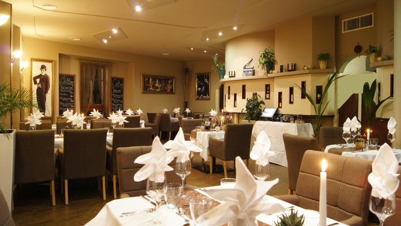 Elegantes Restaurant mit gedeckten Tischen, Kerzenlicht und dekorativen Bildern an den Wänden.