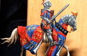 Zinnfigur eines Ritters in Rüstung auf einem Pferd mit buntem Wappenrock.