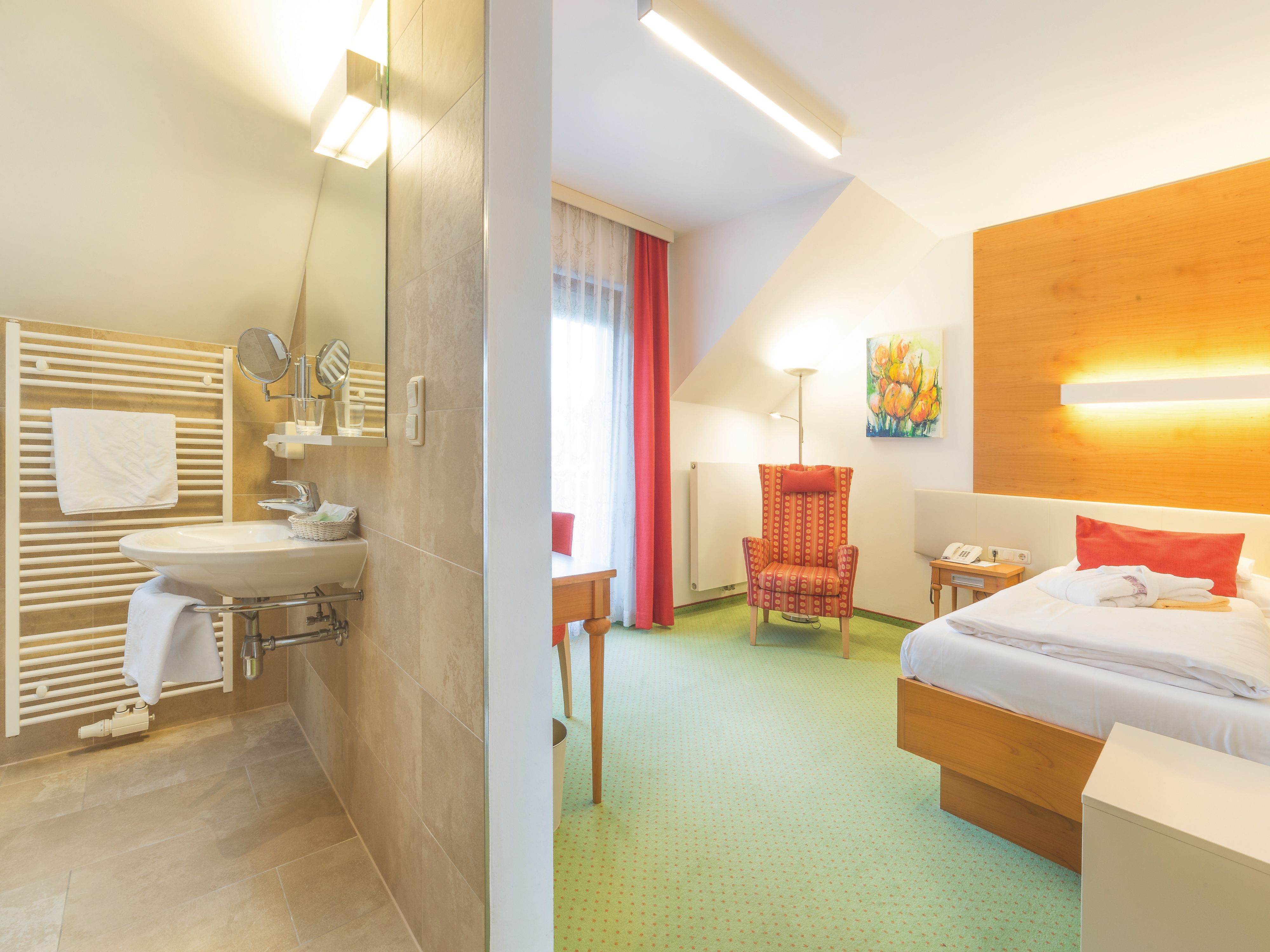Elegantes Hotelzimmer mit modernem Bad, Einzelbett, rotem Sessel und grüner Teppichboden.