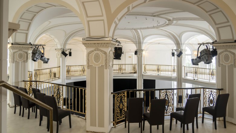 Innenansicht eines eleganten Saals mit Bögen und goldenen Geländern.