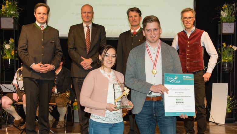 Gruppe von Menschen bei einer Preisverleihung, zwei Personen halten eine Trophäe und eine Urkunde.